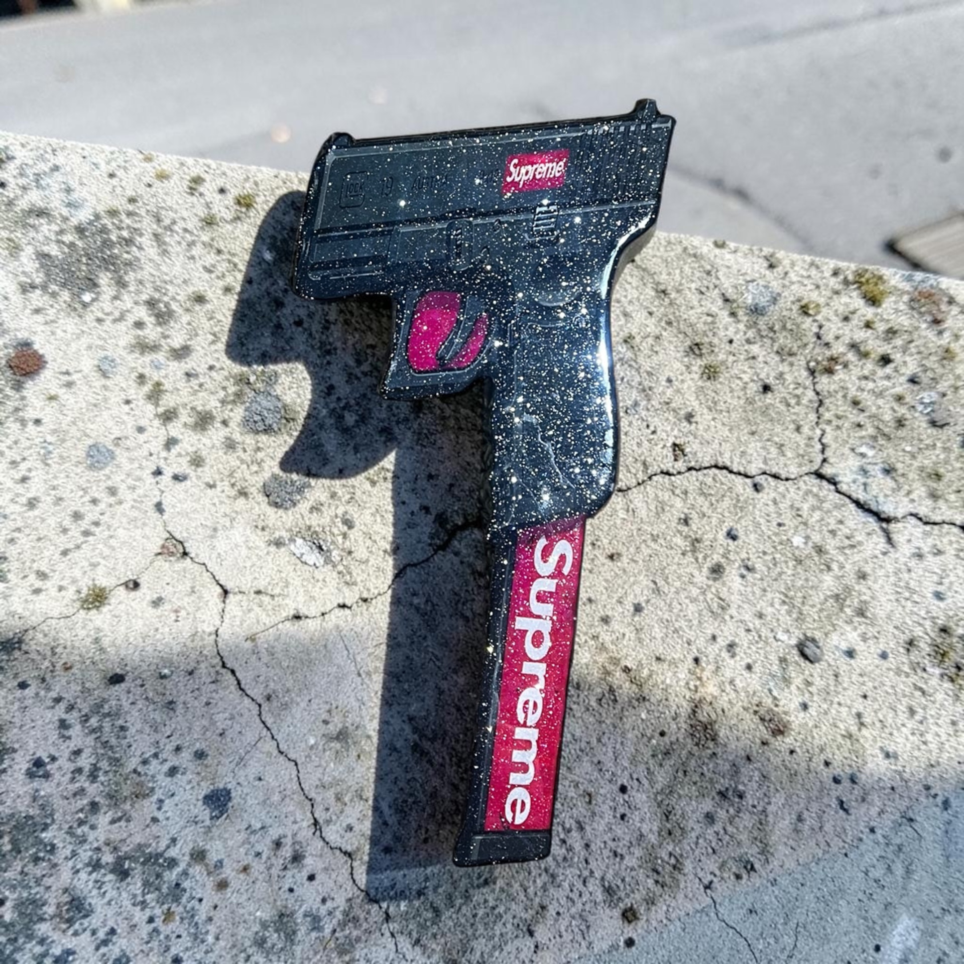 Custom hand-cut and epoxy Supreme gun wall art piece on wood with glossy black resin finish, white speckle detail, and red Supreme branding